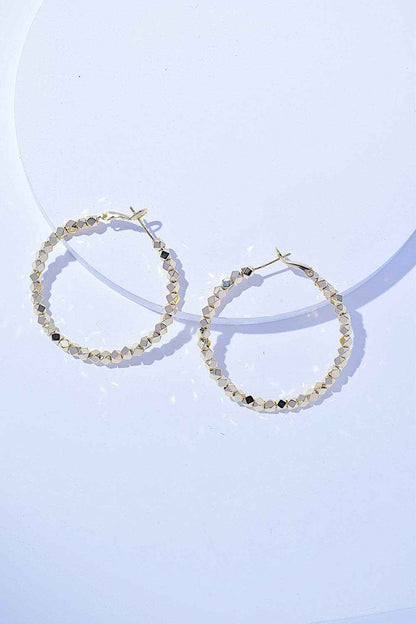 Pair of shiny alloy hoop earrings with textured surface on light background