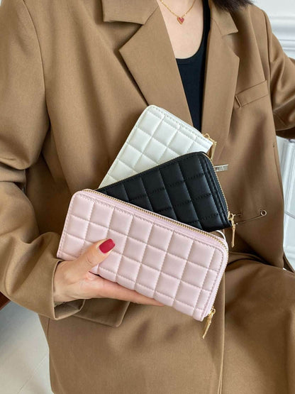 Three small PU leather wallets in white, black, and pink with quilted design held by a person wearing a brown blazer