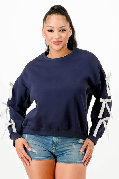 Woman wearing navy casual sweatshirt with bow details on sleeves and denim shorts